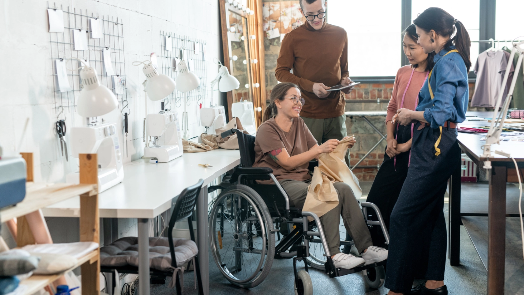Eine Gruppe junger Modedesigner umringt eine gehandicapte Näherin im Rollstuhl bei der Besprechung der wichtigsten Punkte der neuen Kollektion,