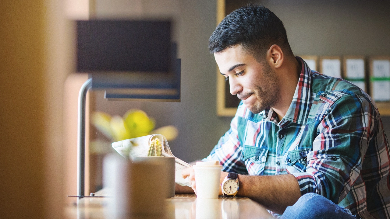 Ein junger Mann liest Zeitung und trinkt dabei Kaffee.
