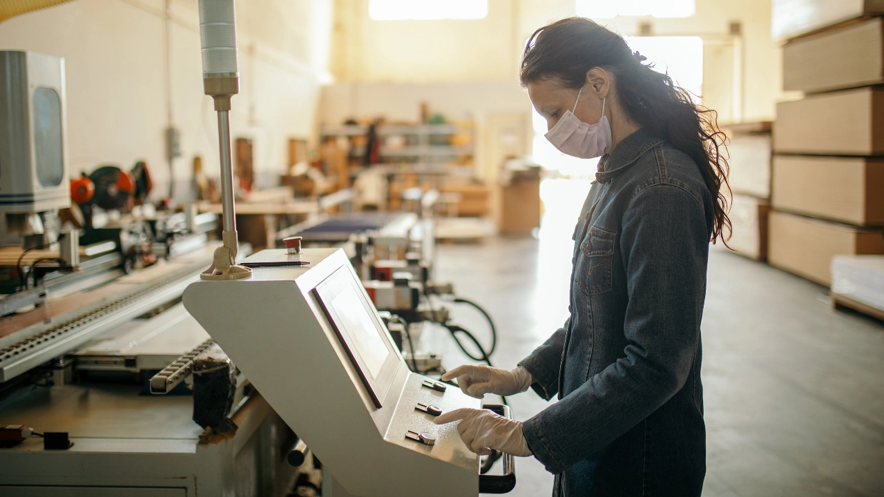 Frau arbeitet mit Mundschutz in einem Industriebetrieb an einer Maschine