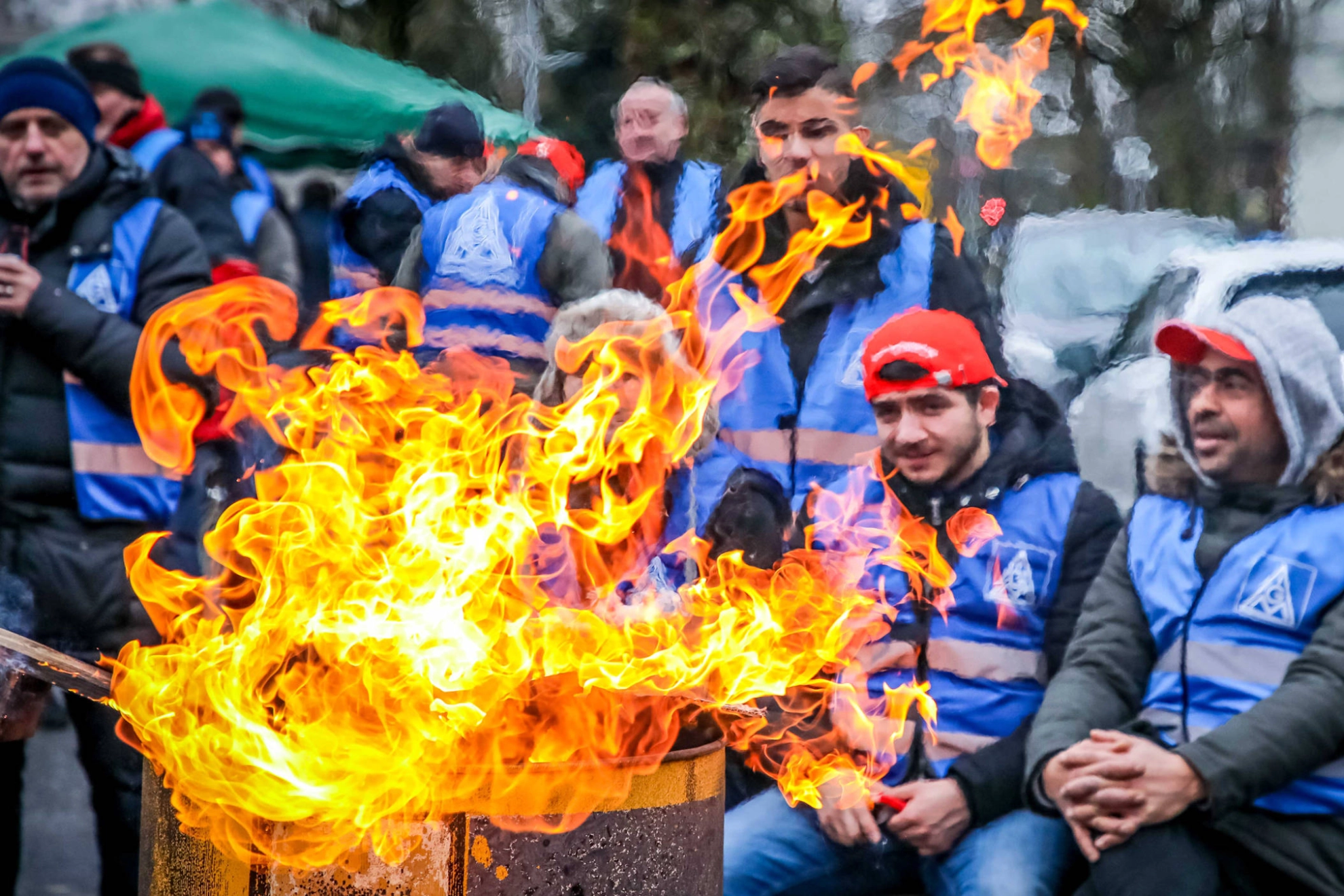 Mehrere junge Männer sitzen an einer Feuertonne.