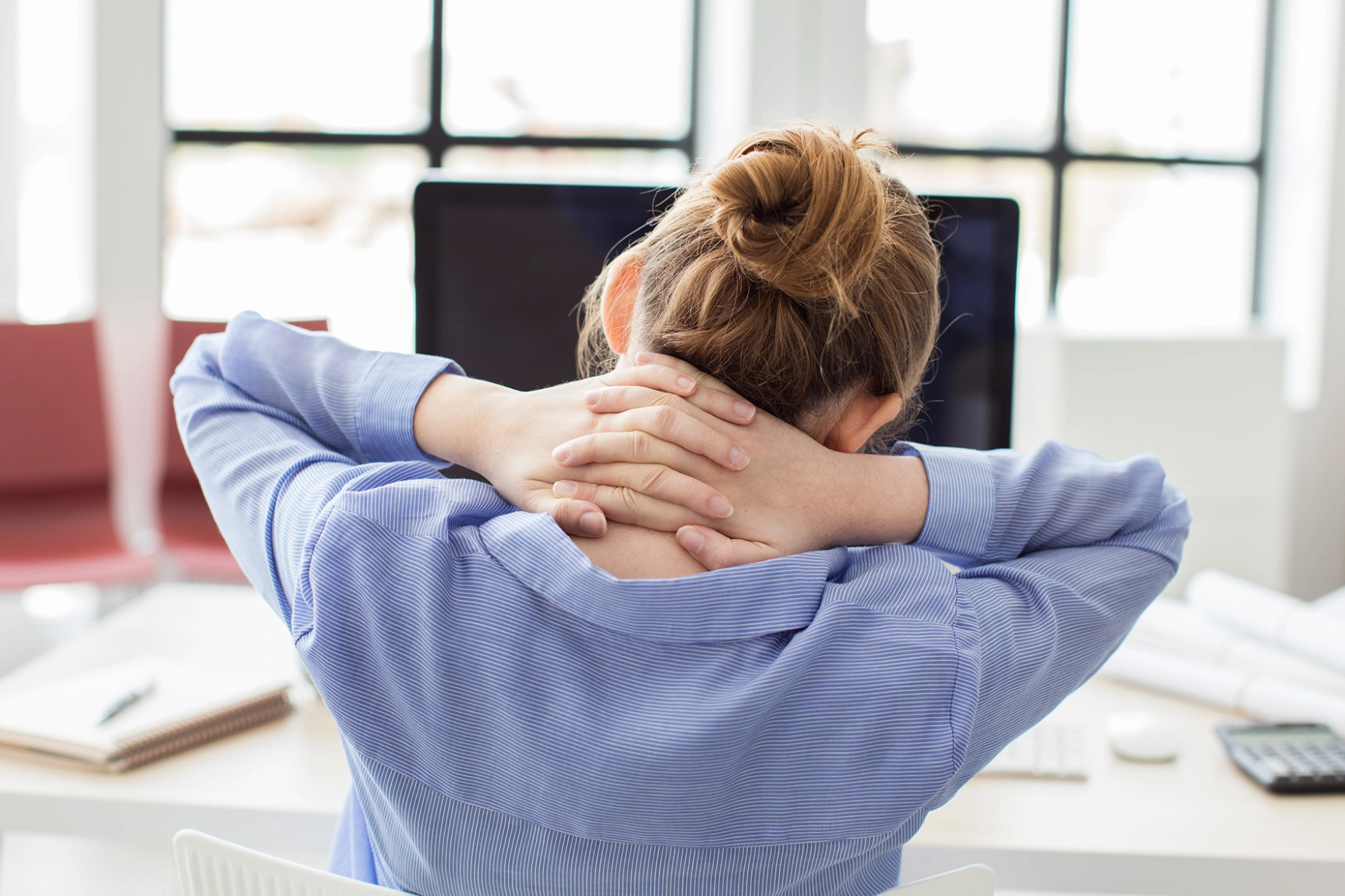 Eine Frau an einem Computerarbeitsplatz hat Nacken- und Rückenschmerzen
