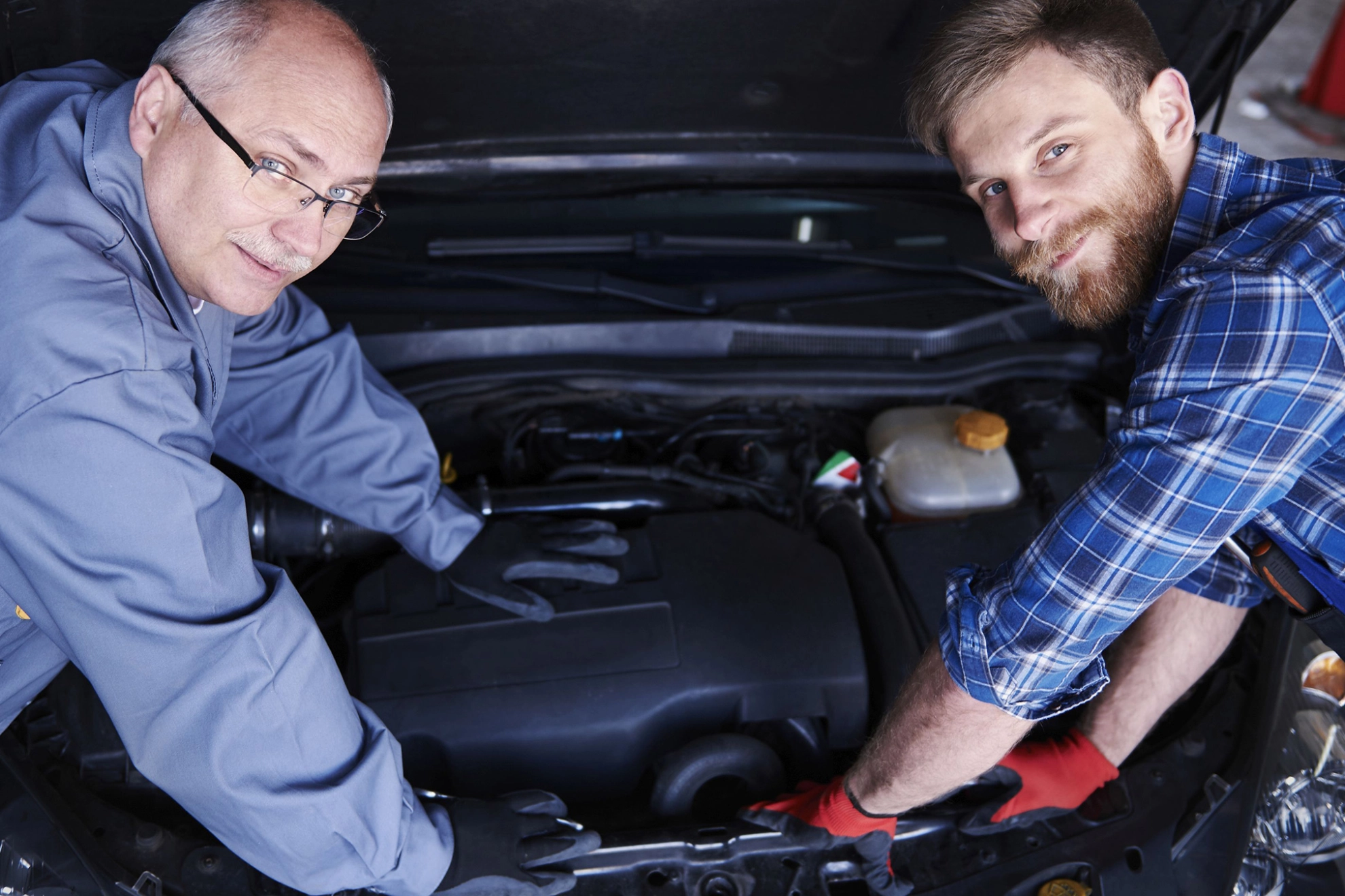 Zwei Kfz-Mechaniker inspizieren den Motorraum eines Autos