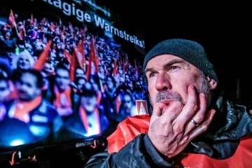 Ein Mann mit Mütze und Streikweste pfeift durch die Finger.